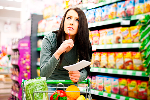 Mujer joven en el supermercado con una lista en la mano, con actitud pensativa, decidiendo qué comprar.